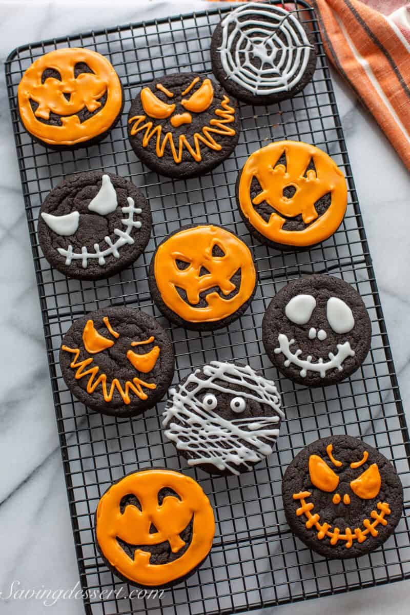 An overhead photo of a cooling rack filled with dark black cocoa cookies decorated in white and orange icing for Halloween.