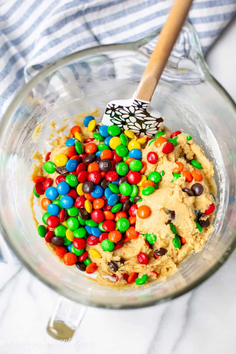 A bowl of cookie dough with M&M's being folded in.
