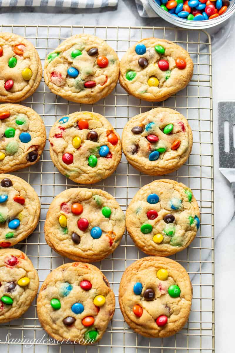 M&M Cookies on a cooling rack with a bowl of M&M's on the side.