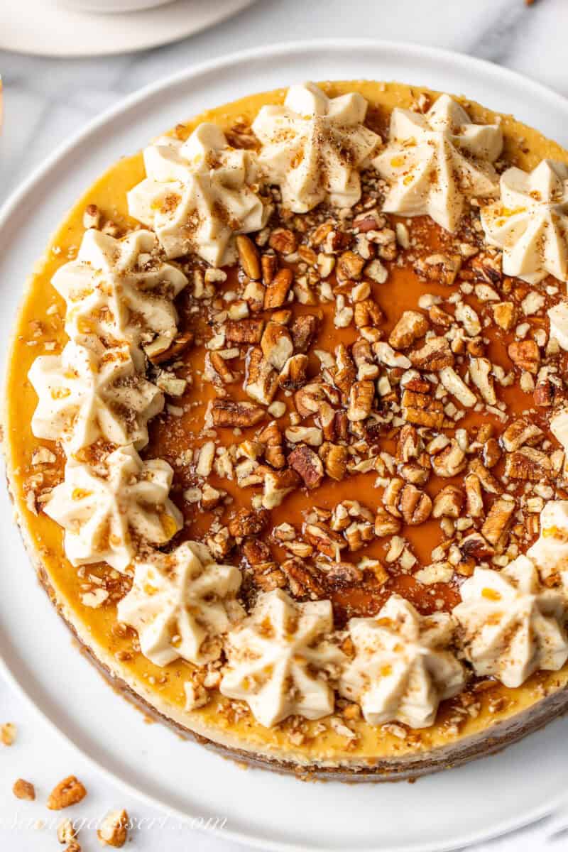 An overhead photo of a maple cheesecake with maple buttercream swirls, pecans and maple syrup.