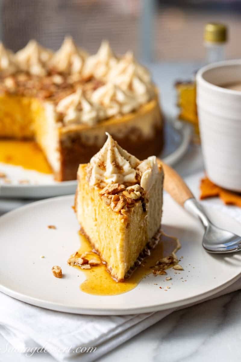 A thin slice of maple cheesecake on a plate with a drizzle of maple syrup and chopped pecans on top.