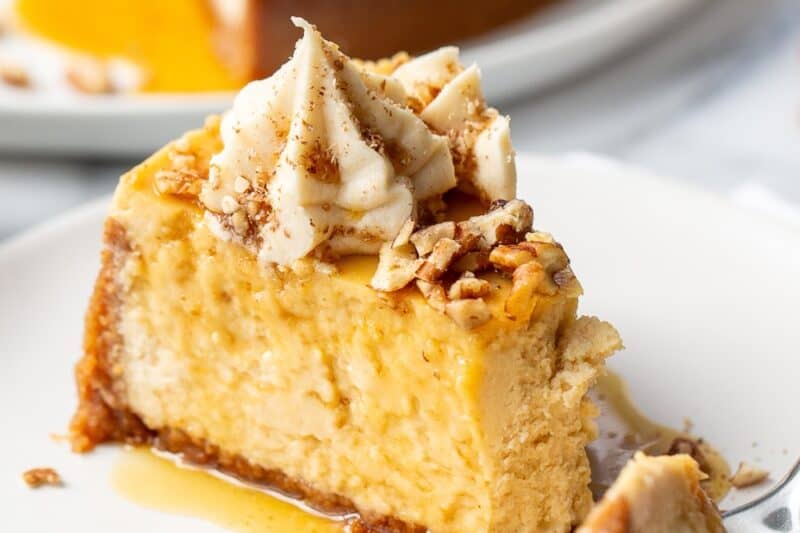 A slice of maple cheesecake on a plate with the front corner cut off with a fork.
