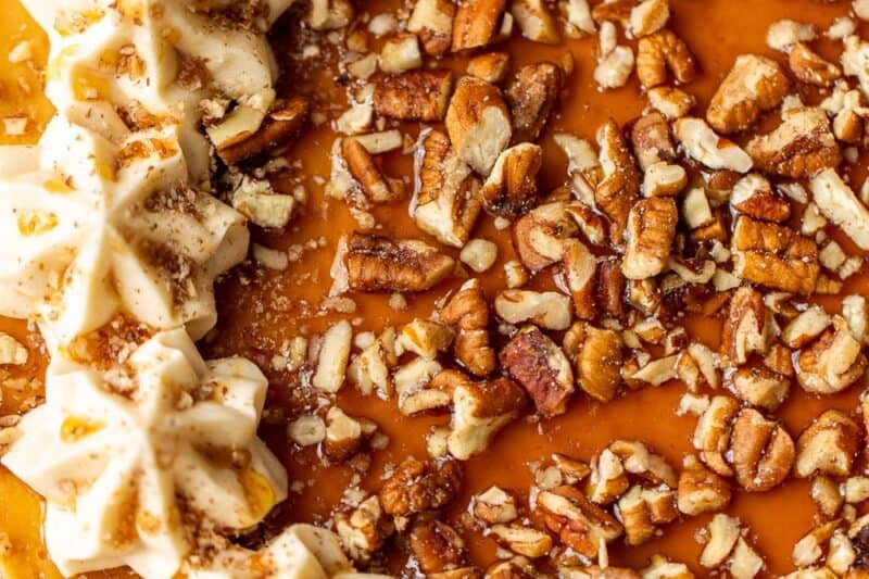 An overhead shot of a whole maple cheesecake decorated with swirls of maple buttercream, maple syrup and pecans.