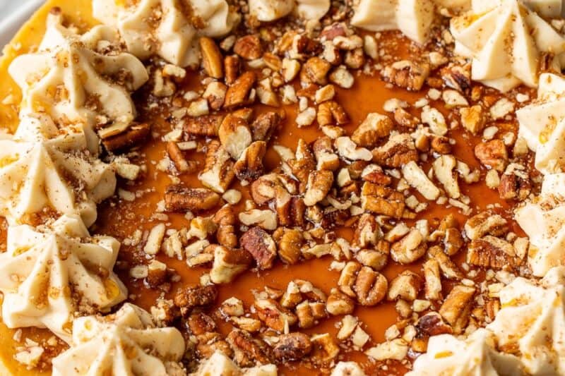 An overhead shot of a whole maple cheesecake decorated with swirls of maple buttercream, maple syrup and pecans.