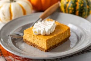 Pumpkin Cheesecake Bar topped with swirly whipped cream on a plate.
