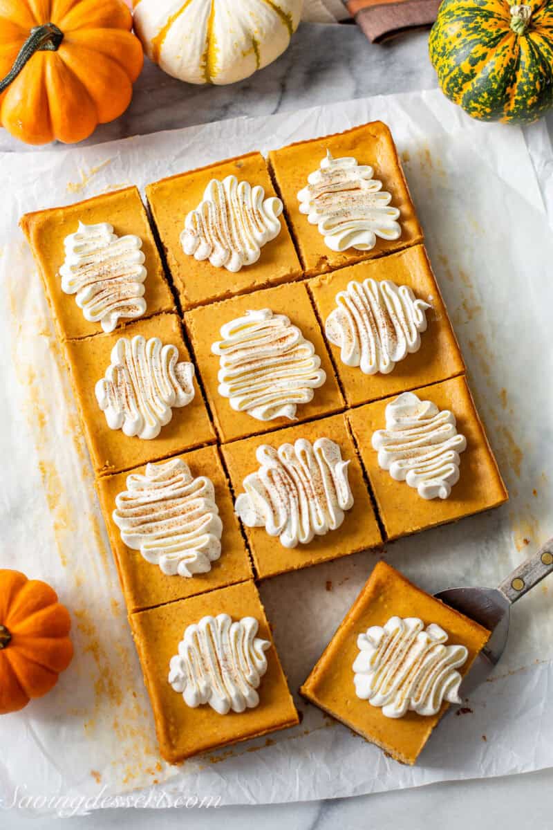 An overhead shot of a dozen squares of pumpkin cheesecake with whipped cream on top.