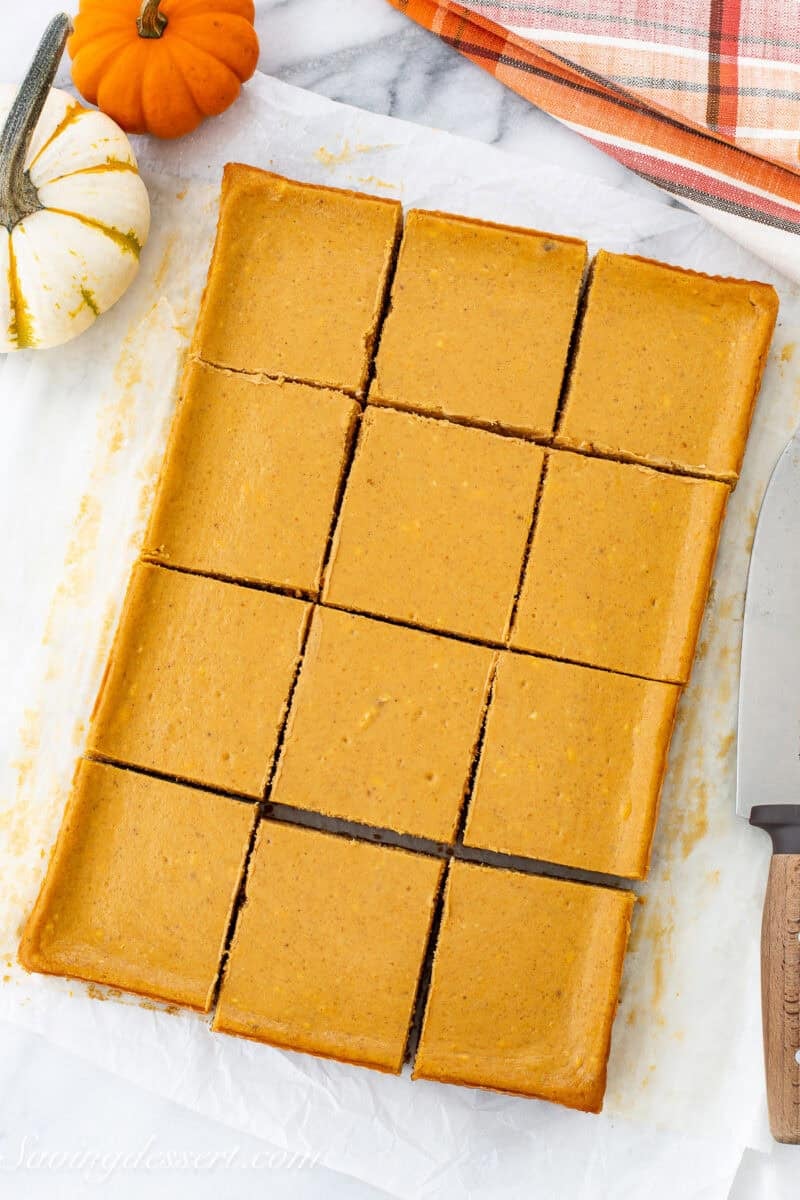 An overhead view of a pan of pumpkin cheesecake bars cut into squares.