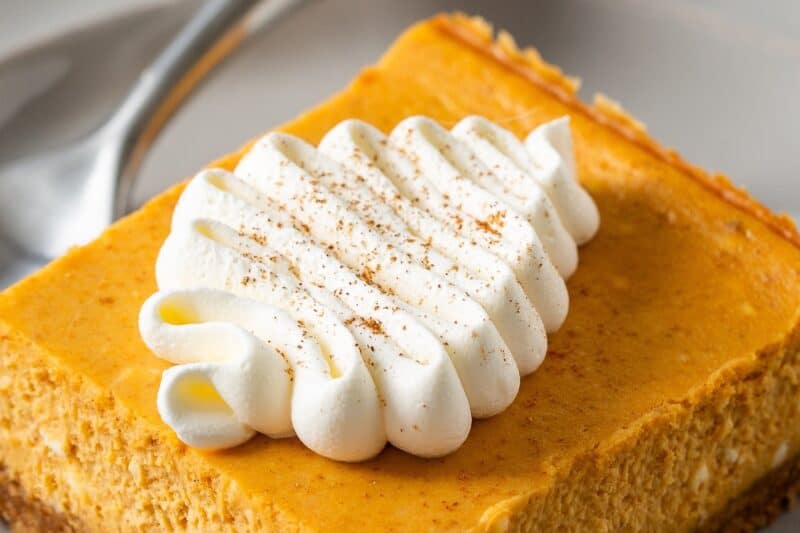 A square piece of pumpkin cheesecake on a plate with a fork.