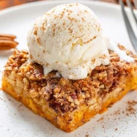 A closeup photo of a piece of pumpkin dump cake with a scoop of vanilla ice cream on top.