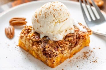 A closeup photo of a piece of pumpkin dump cake with a scoop of vanilla ice cream on top.