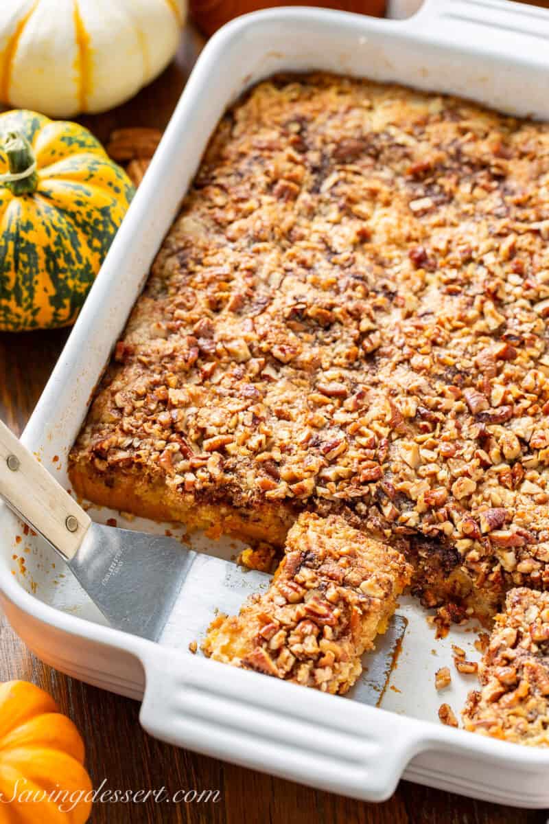 A pan of pumpkin dump cake with chopped pecans on top and a spatula scooping out a piece.