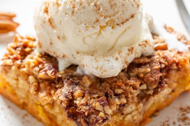 A slice of pumpkin dump cake on a plate topped with ice cream and a dusting of pumpkin spice.