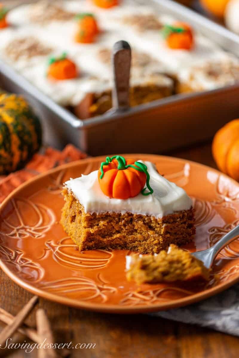 A side view of a piece of pumpkin spice cake cut with a fork and decorated with a fondant pumpkin.