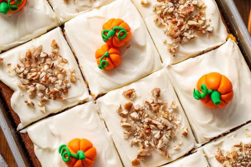 An overhead of a pan of pumpkin spice cake decorated with fondant pumpkins and chopped pecans.