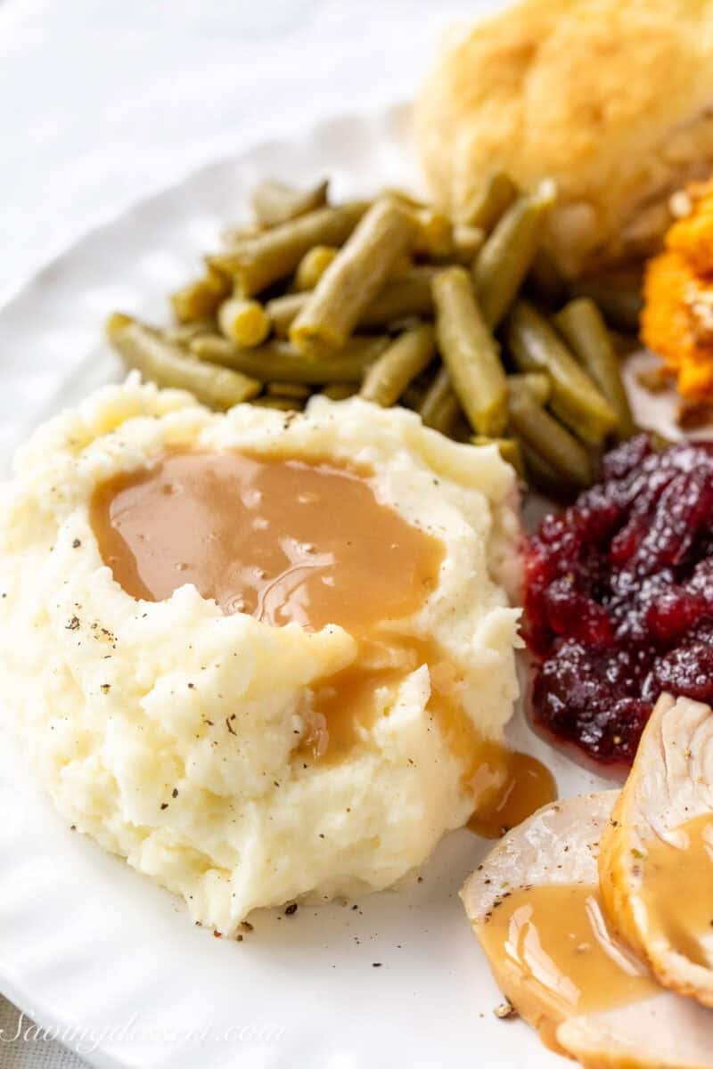 A mound of mashed potatoes and gravy on a plate with green beans and turkey.