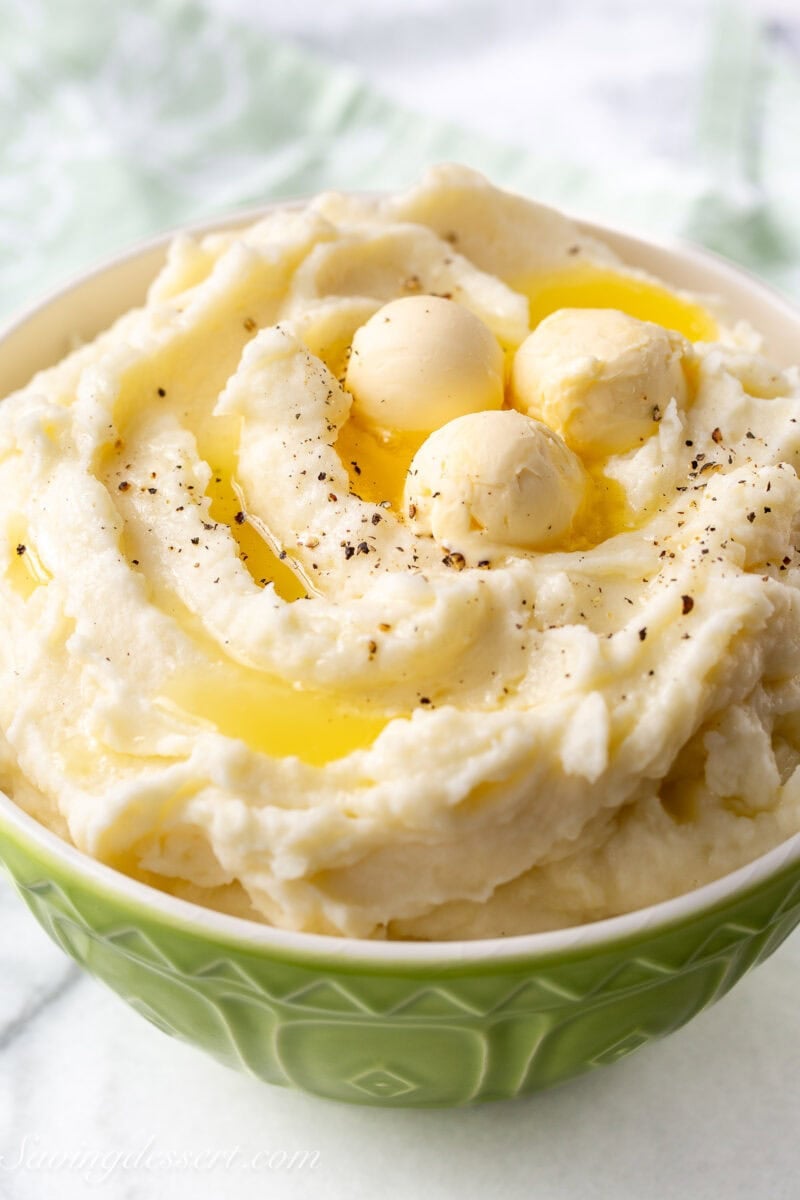 A side view of a bowl of mashed potatoes with scoops of butter melting on top.