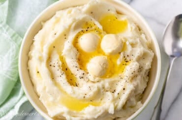 An overhead view of a bowl of mashed potatoes with butter and black pepper on top.
