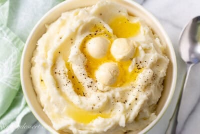 An overhead view of a bowl of mashed potatoes with butter and black pepper on top.