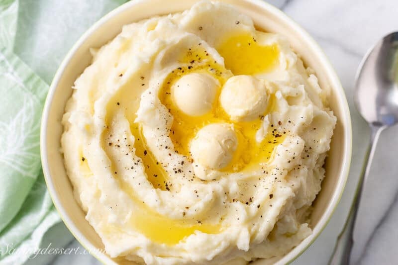 An overhead view of a bowl of mashed potatoes with butter and black pepper on top.