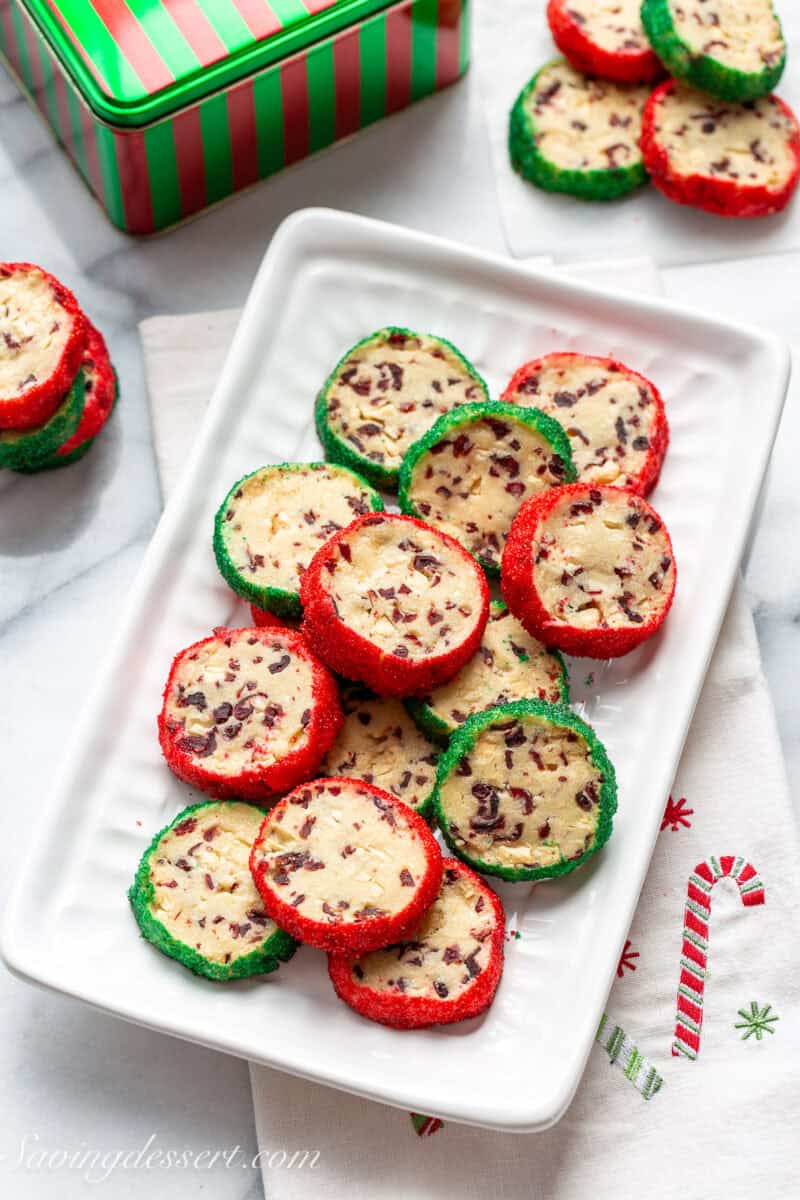 An overhead photo of a platter filled with cranberry white chocolate shortbread cookies decorated with red and green coarse sugar.
