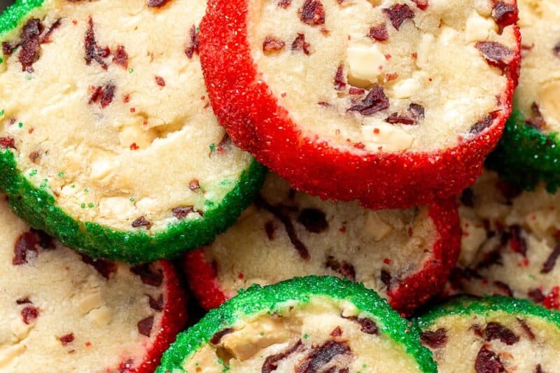 A closeup of a cookie tin filled with cranberry shortbread cookies trimmed in red and green sanding sugar.