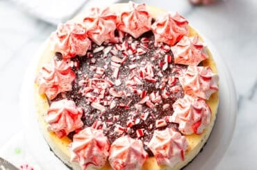 An overhead view of a whole peppermint cheesecake topped with chocolate ganache and crushed peppermint candy.