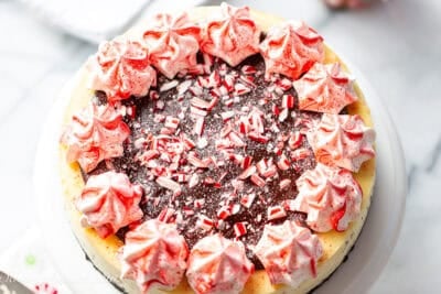 An overhead view of a whole peppermint cheesecake topped with chocolate ganache and crushed peppermint candy.