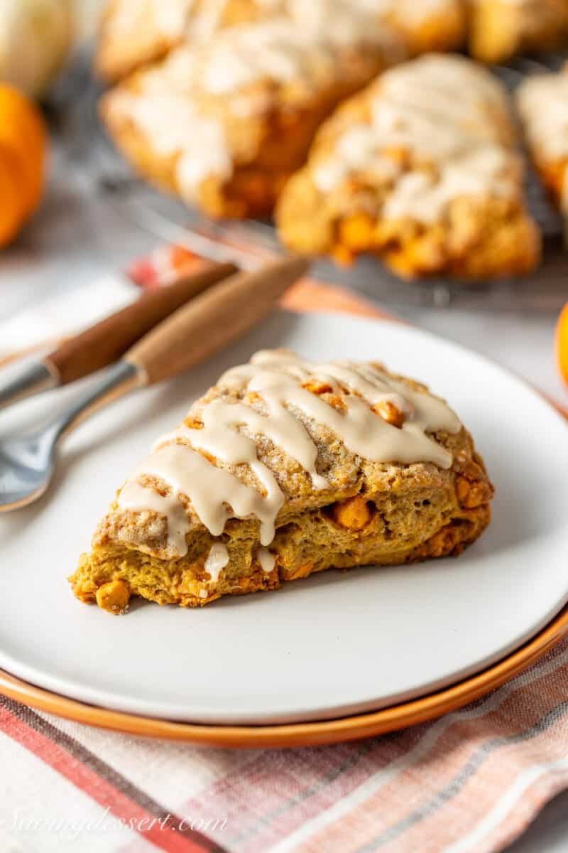 An iced pumpkin scone on a plate with more in the background.