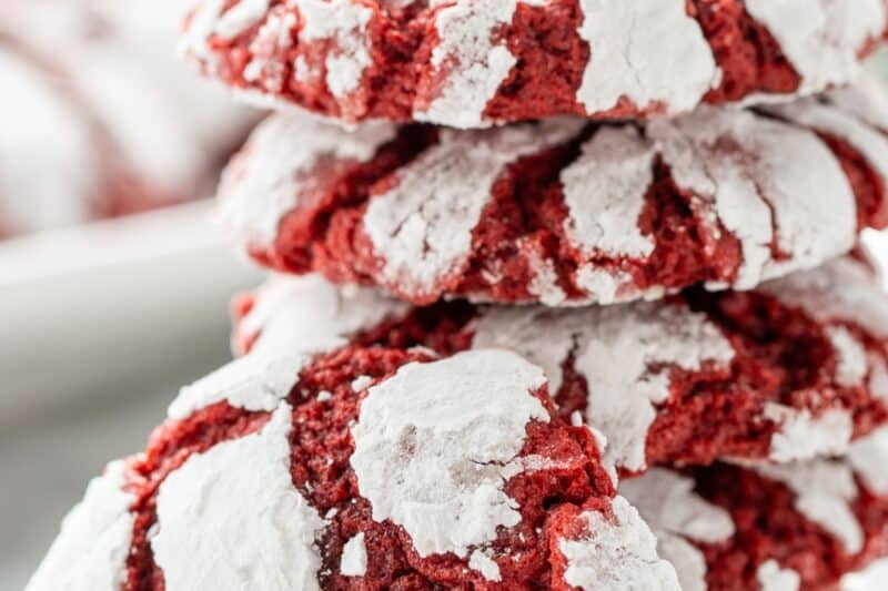 A closeup of a stack of red velvet crinkle cookies with one propped up on the side.