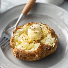 A plate with an air-fryer baked potato split open and topped with a ball of butter and black pepper.