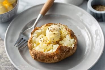 A plate with an air-fryer baked potato split open and topped with a ball of butter and black pepper.