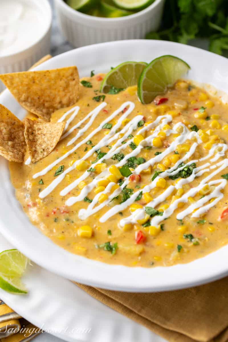 A bowl of Mexican Street Corn Chowder topped with Mexican crema, tortilla chips, cilantro and lime wedges.
