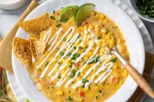 An overhead view of a bowl of Mexican Street Corn Chowder topped with a sour cream drizzle and chips.