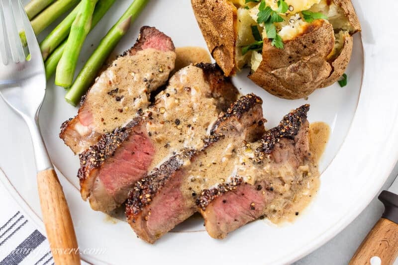 Sliced Steak Au Poivre on a plate topped with brandy cream sauce