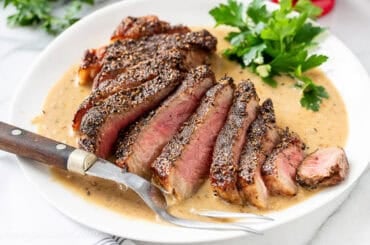 A sliced steak on a platter over brandy cream sauce.