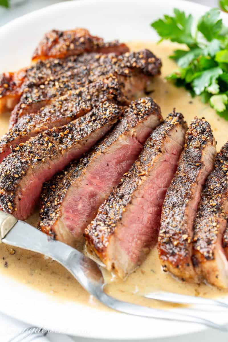 Sliced pepper crusted steak au poivre on a platter with brandy cream sauce.
