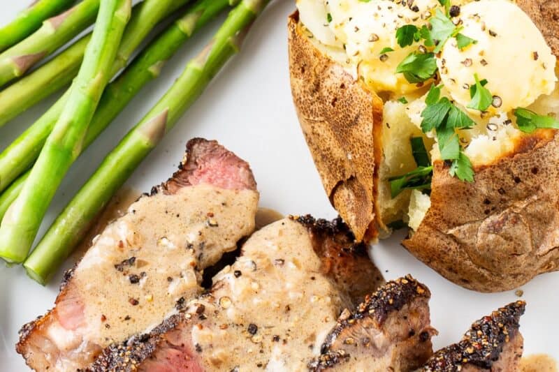 An overhead shot of a plate of sliced steak au poivre drizzled with a brandy cream sauce.