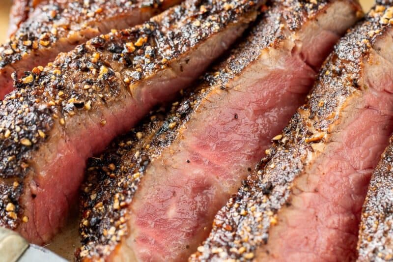 Sliced Steak Au Poivre on a platter filled with bandy cream sauce.