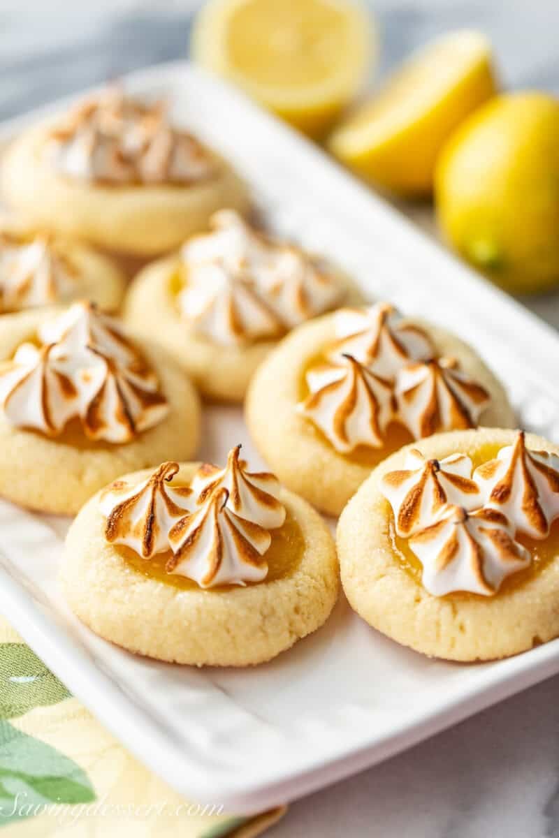 A small platter filled with lemon meringue pie cookies with lemons in the background.