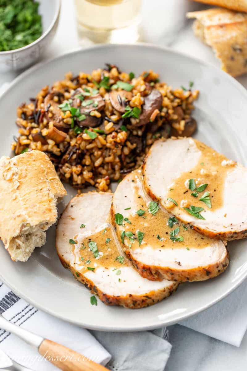 A plate with sliced pork loin, bread and mushroom wild rice pilaf.