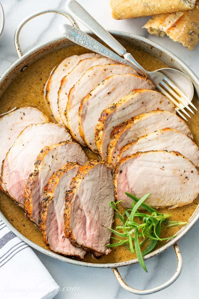A round pan filled with golden sauce and sliced pork loin roast.