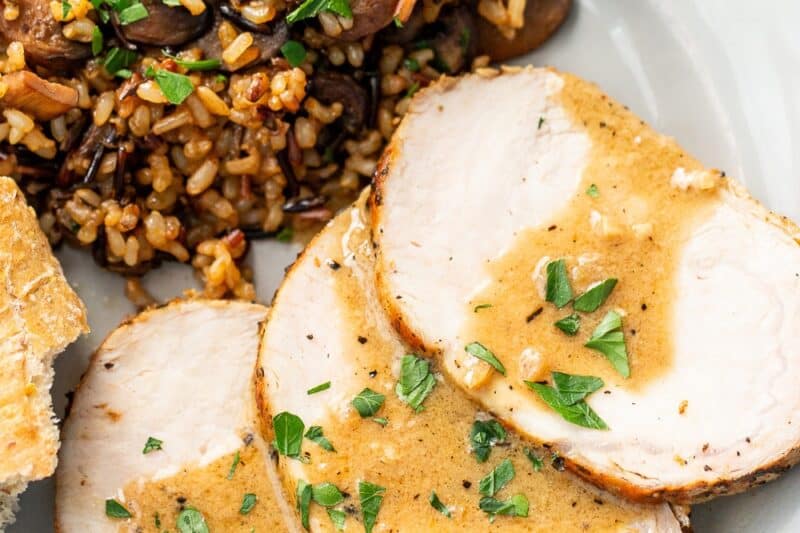 An overhead view of a plate with sliced pork loin roast, mushroom pilaf and a piece of bread on the side.