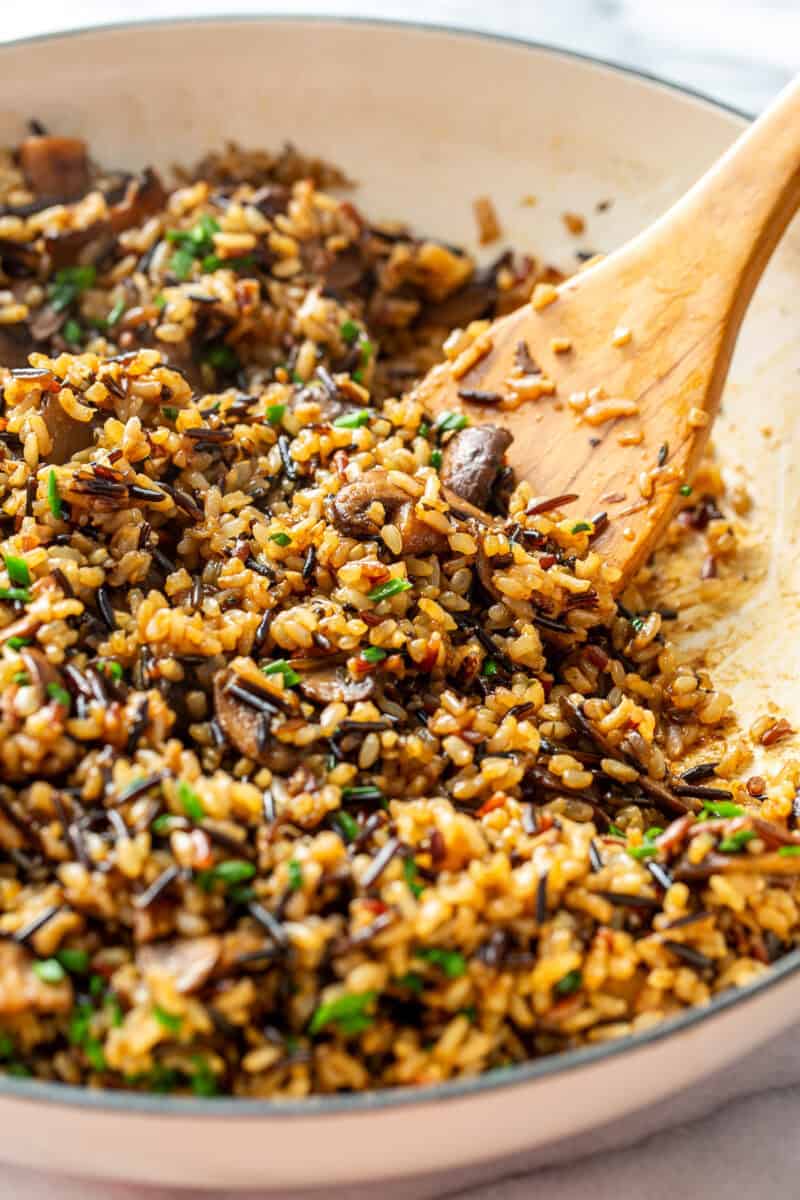 A skillet filled with mushrooms and a wild rice blend being stirred with a wooden spoon.