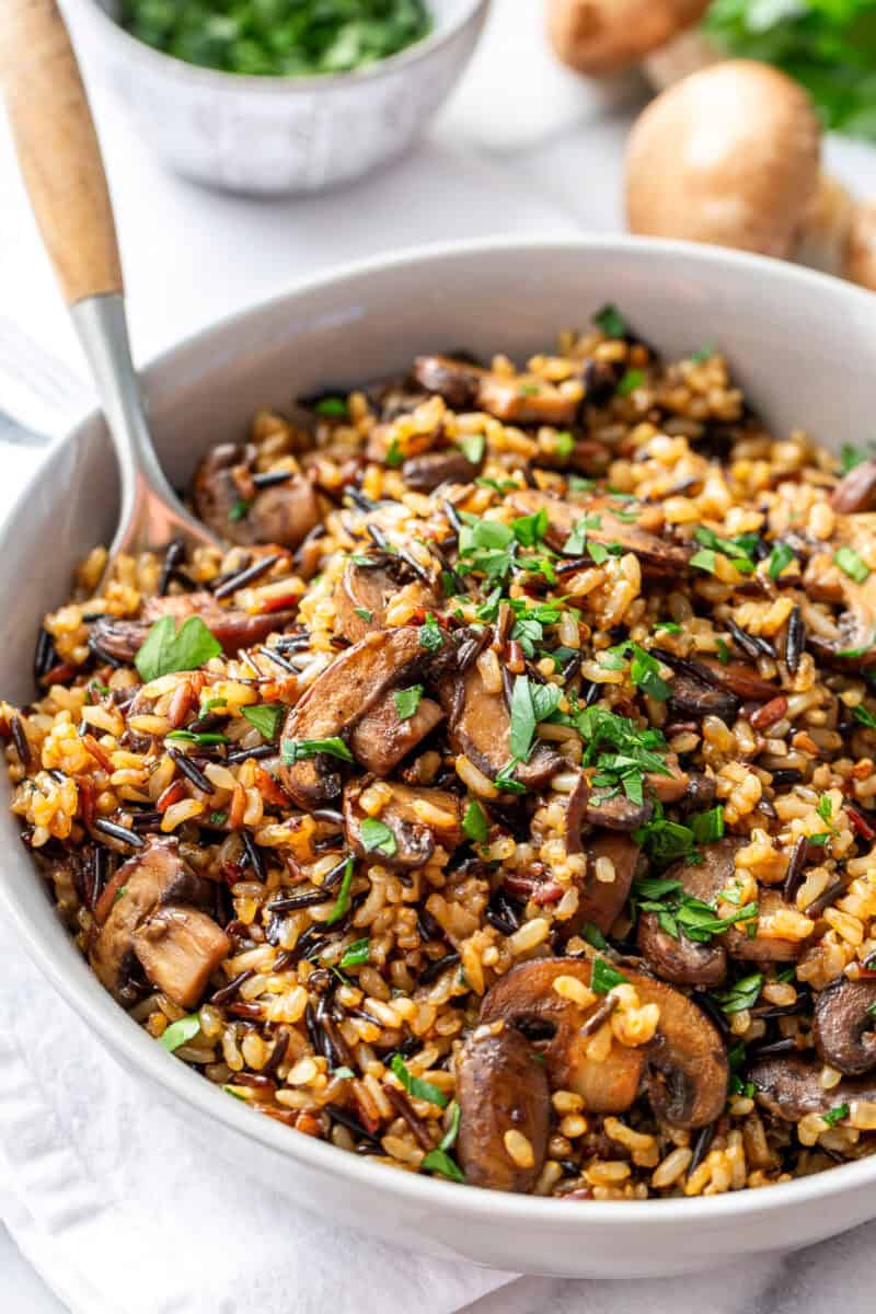 A gray bowl of wild rice and mushroom pilaf with a spoon and parsley garnish.