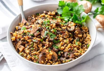 A large bowl of wild rice mushroom pilaf with a spoon and parsley garnish.