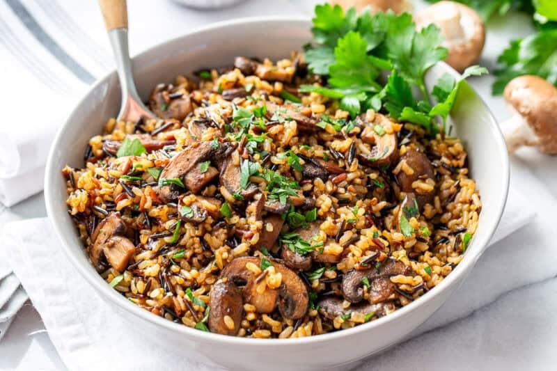 A large bowl of wild rice mushroom pilaf with a spoon and parsley garnish.