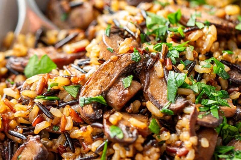 A close up shot of a bowl of mushrooms and a wild rice blend with a spoon and parsley garnish.