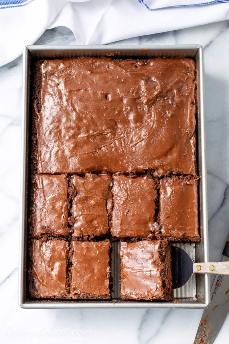 An overhead view of a full pan of buttermilk chocolate cake with half the pan sliced into individual pieces.