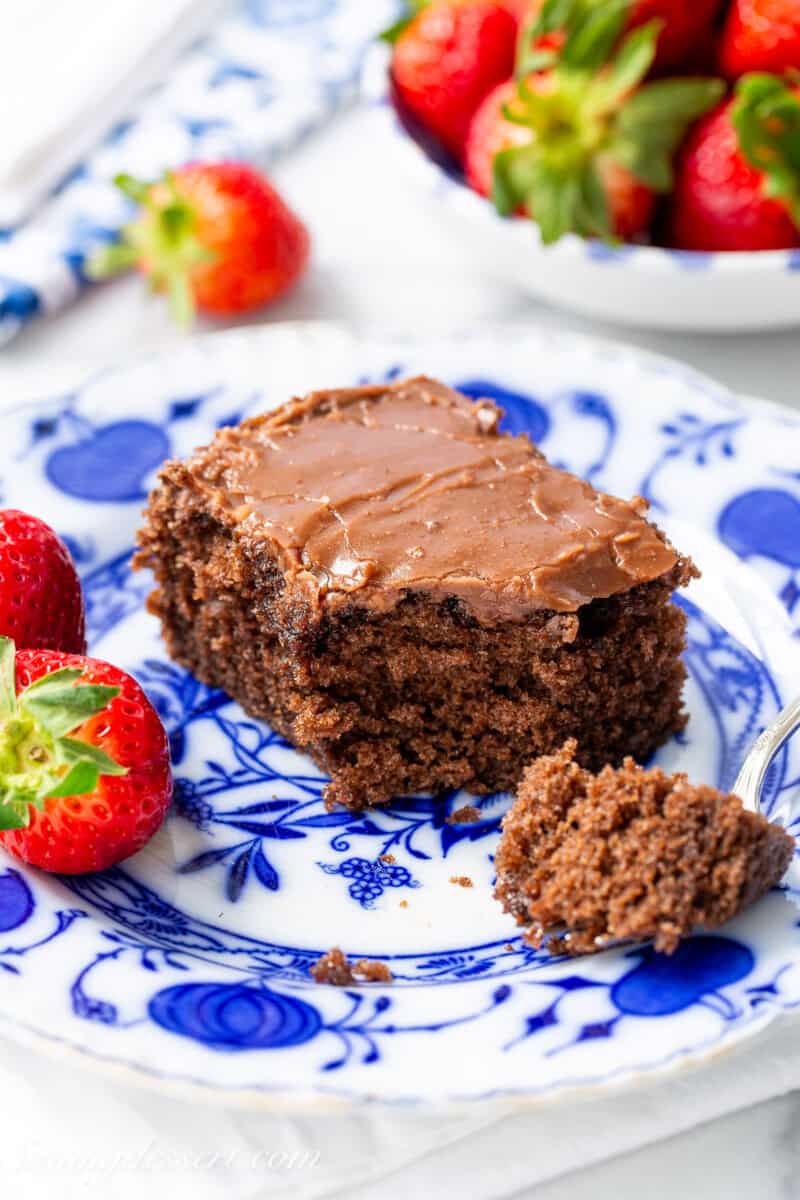 A side view of a piece of buttermilk chocolate cake on a blue plate with strawberries on the side.