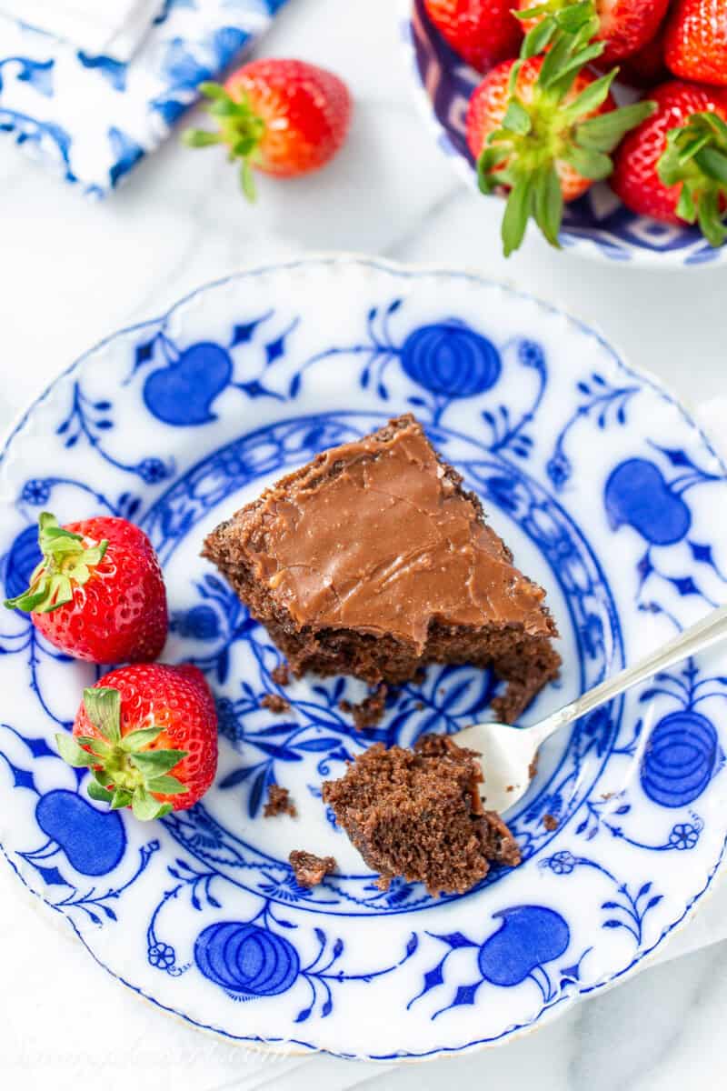 An overhead view of a piece of chocolate cake on a blue plate with strawberries on the side.
